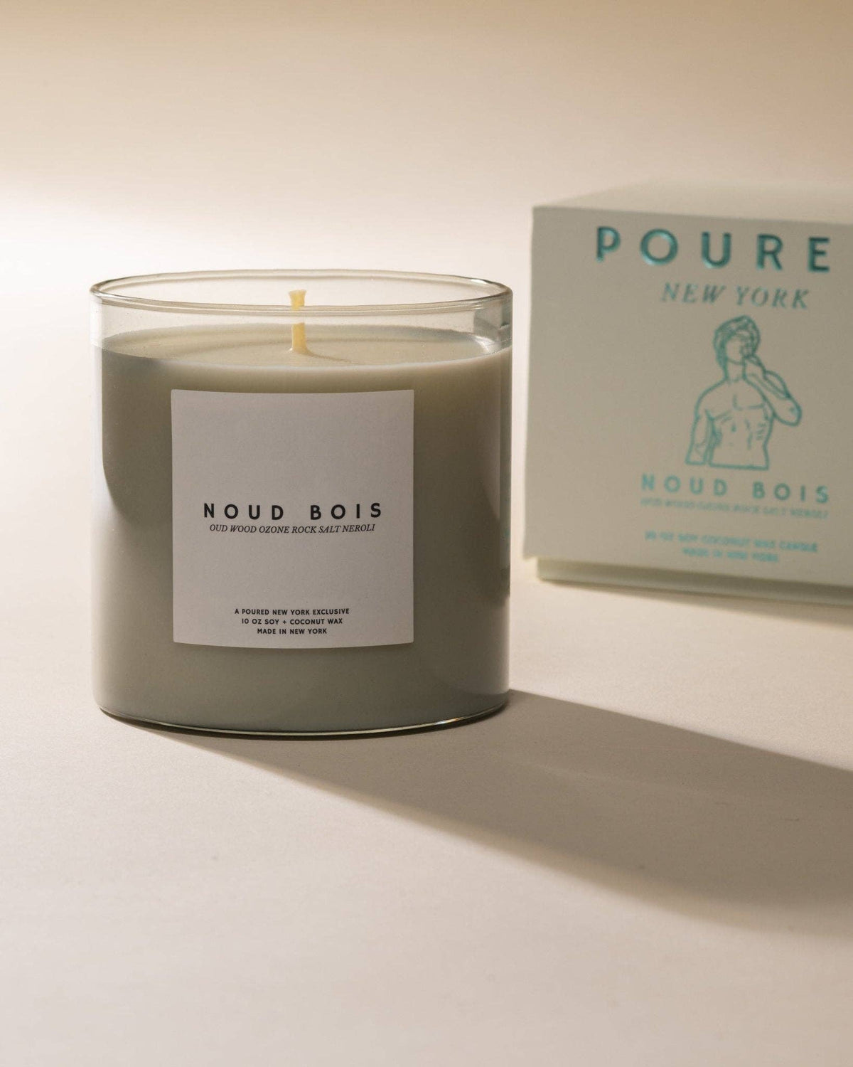 Noud Bois candle in a sage glass jar next to its pale blue Poured gift box