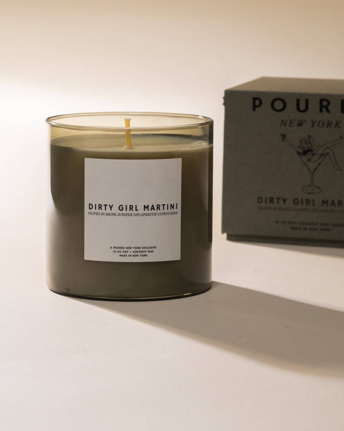 Dirty Girl Martini candle in a dark glass jar next to its gray Poured gift box
