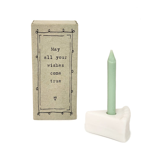Tiny porcelain cake slice with green birthday candle next to a ‘May all your wishes come true’ gift box