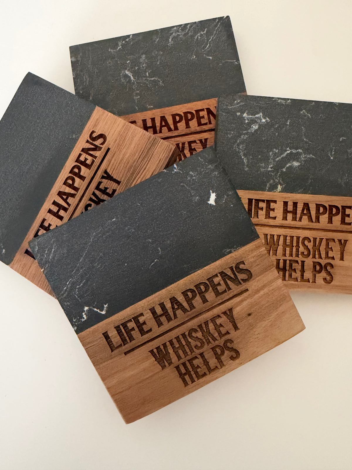 Set of black marble and wood coasters engraved with “Life Happens, Whiskey Helps,” an example of past custom work