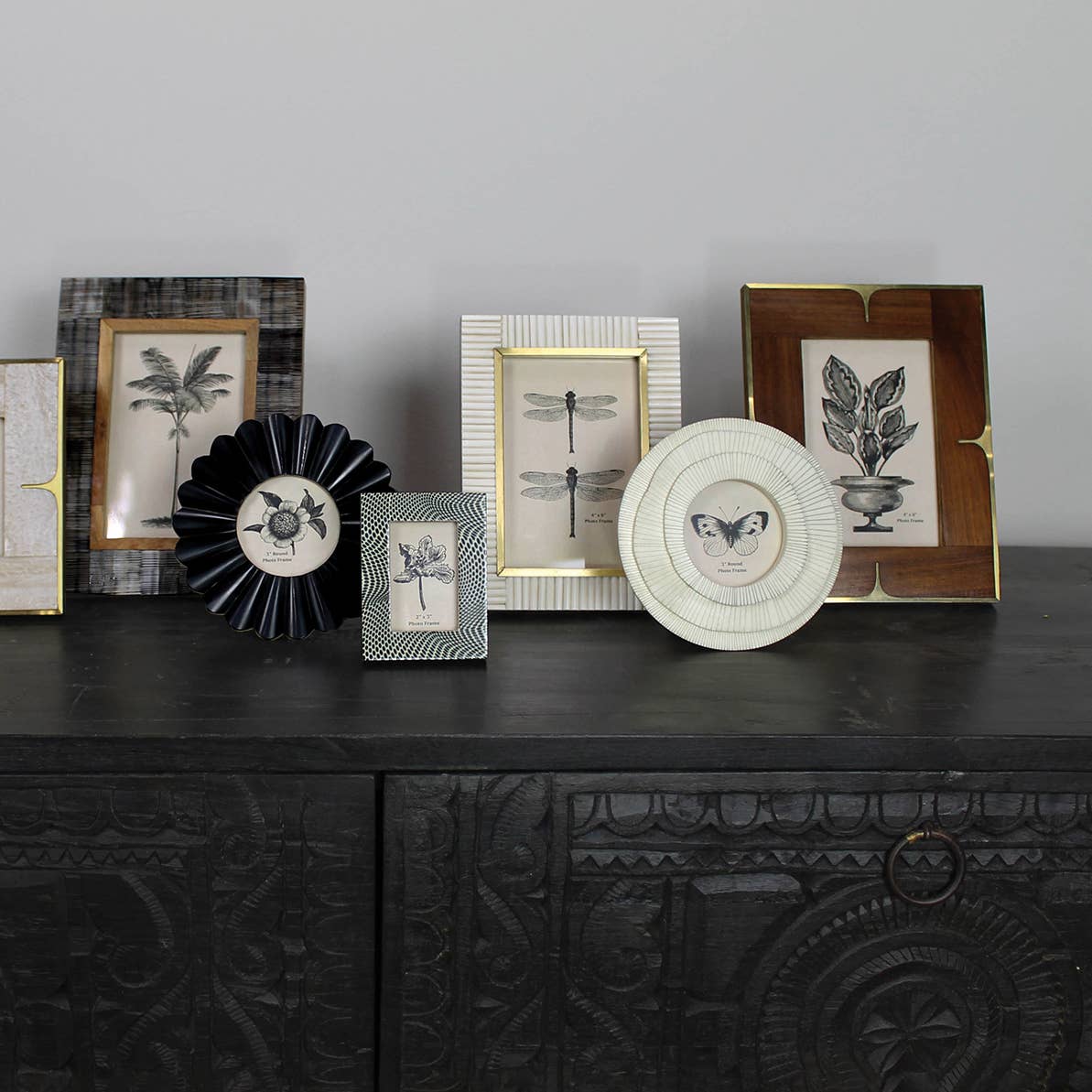 Wood and brass photo frames styled with framed botanical prints on a black sideboard