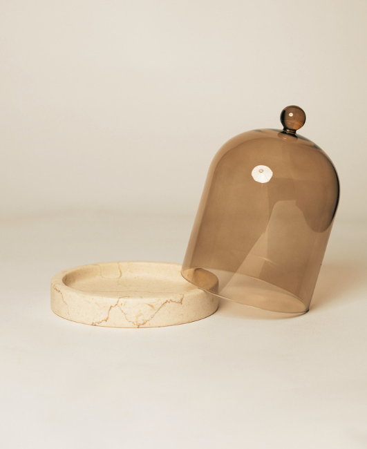 Tinted mushroom-shaped glass candle cloche lifted beside its round travertine coaster base