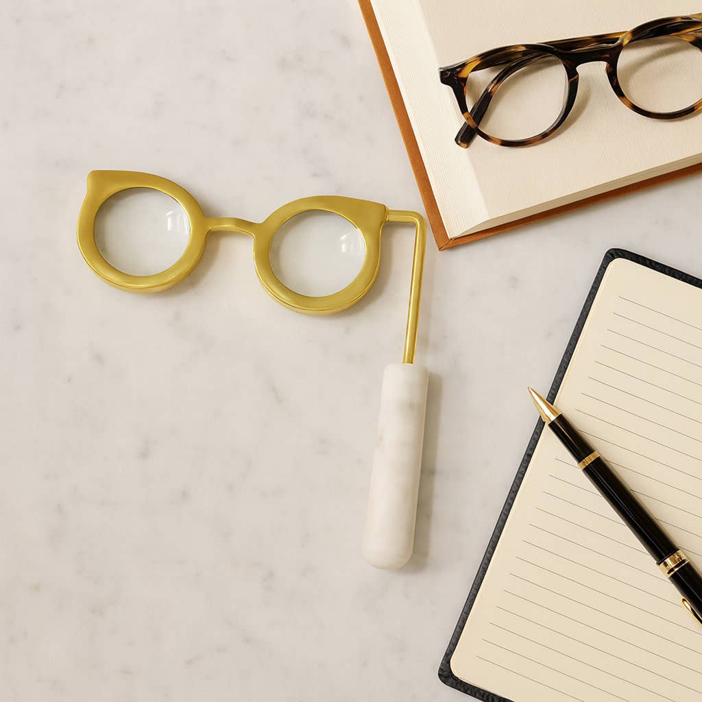 Gold and marble handle magnifying glass styled on a marble surface with a notebook and pen