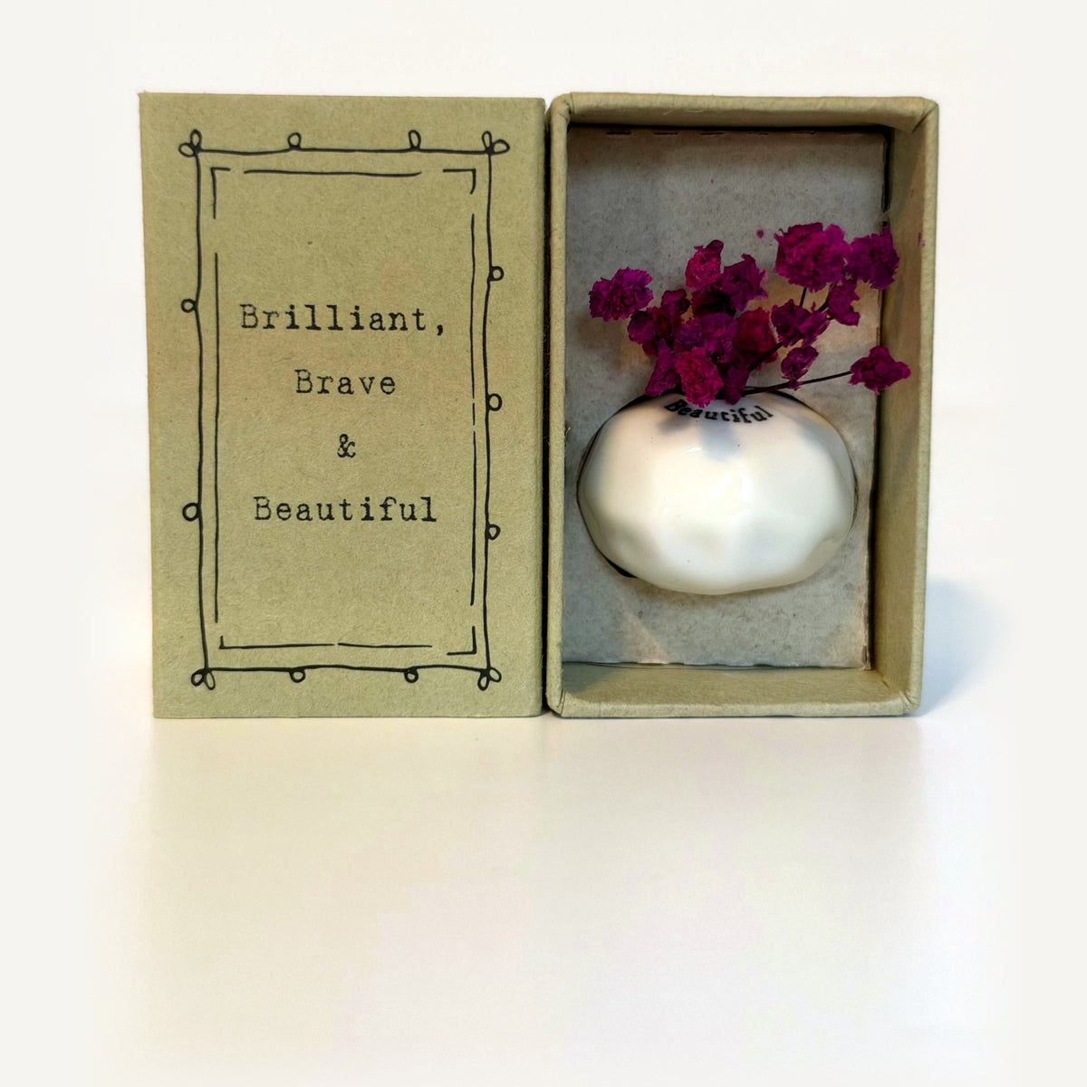 Beautiful tiny vase gift box: white porcelain vase with magenta dried flowers beside a card reading Brilliant, Brave & Beautiful